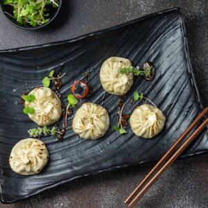 Delicious steamed dumplings garnished with fresh microgreens on a black plate, perfect for food photography.